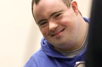 Foto de um jovem com Síndrome de Down sorrindo na direção da câmera