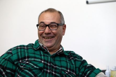 Foto de um homem com cabelos curtos e grisalhos, sorrindo. Ele usa óculos e uma camisa de flanela xadrez verde